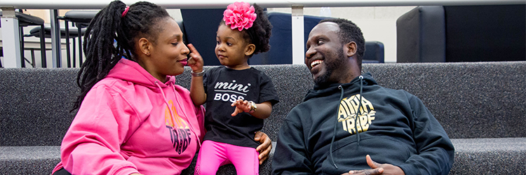 Black/African American family spending time together. A toddler is pointing at her mother while the father looks on smiling.