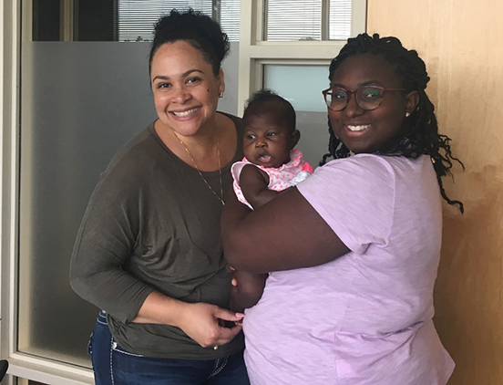 Two smiling women and holding a baby