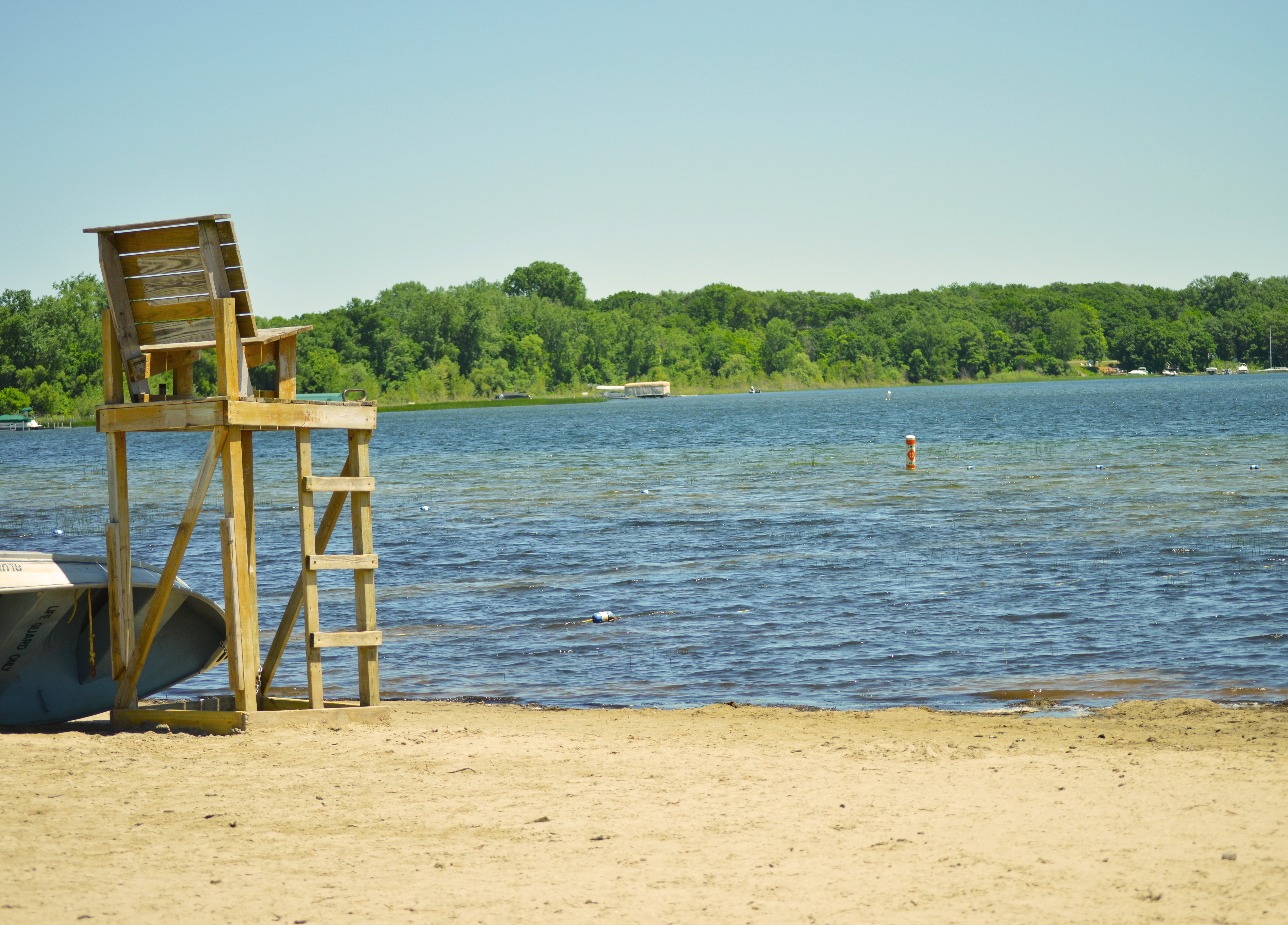 Wooden lifeguard high chair situated on the yellow sand facing the White Bear Lake blue lake.