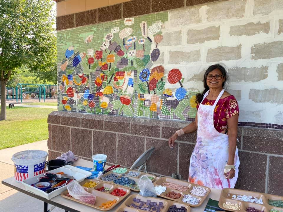 Artist Shakun Maheshwari smiling next to her colorful mosaic artwork at the picnic shelter pillars at McCarrons County Park.