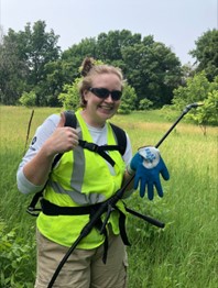 Woman smiling and giving a thumbs up in a field of grass wearing a lime green vest.