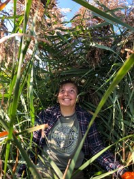 Person dressed in a flannel shirt smiling in a field of foliage 