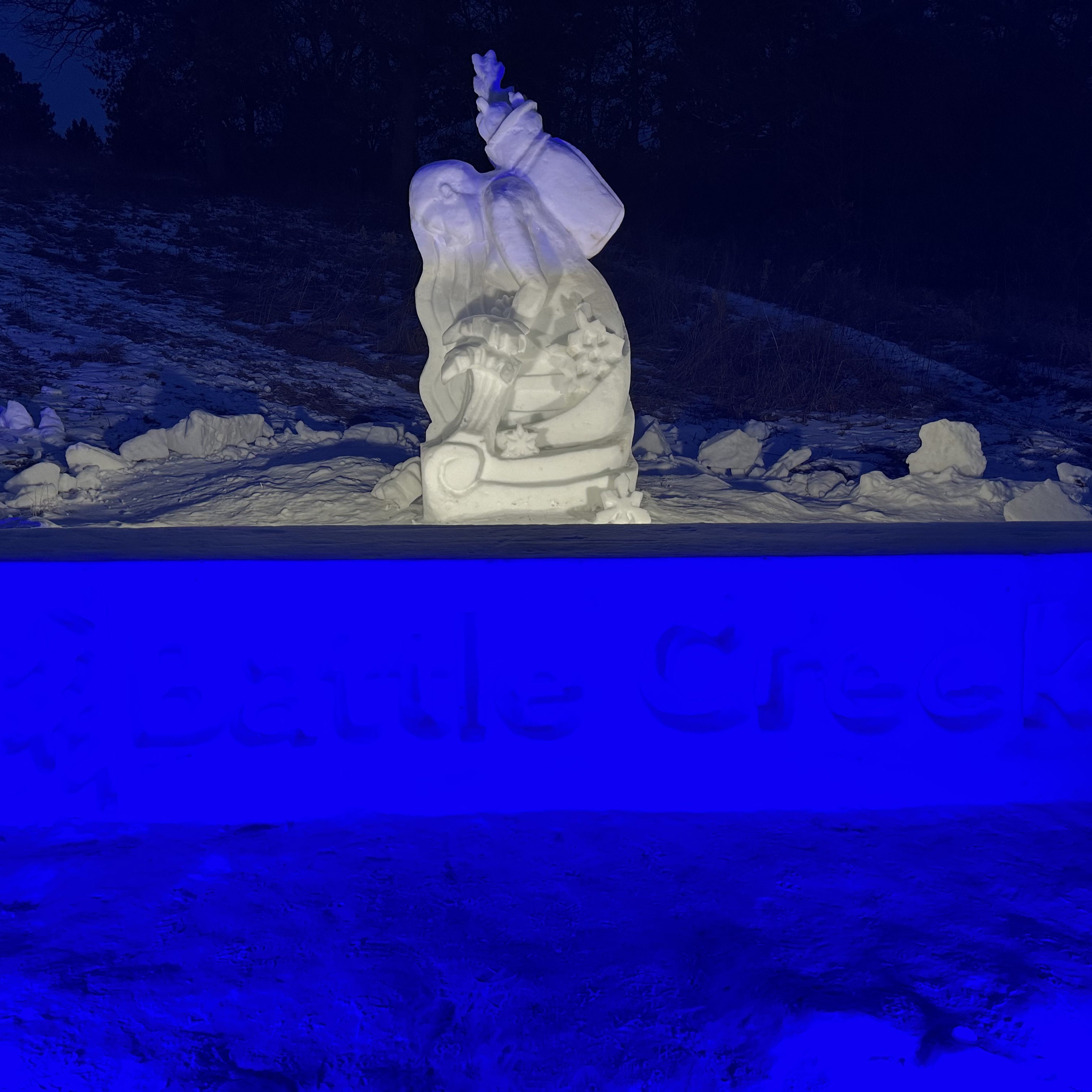 Snow sculpture of a woman kneeling in the snow at the Ramsey county Battle Creek Winter Recreation. Sculpture featured at night with a blue light.