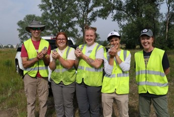 Smiling volunteers in lime green vests holding baby kestral birds.