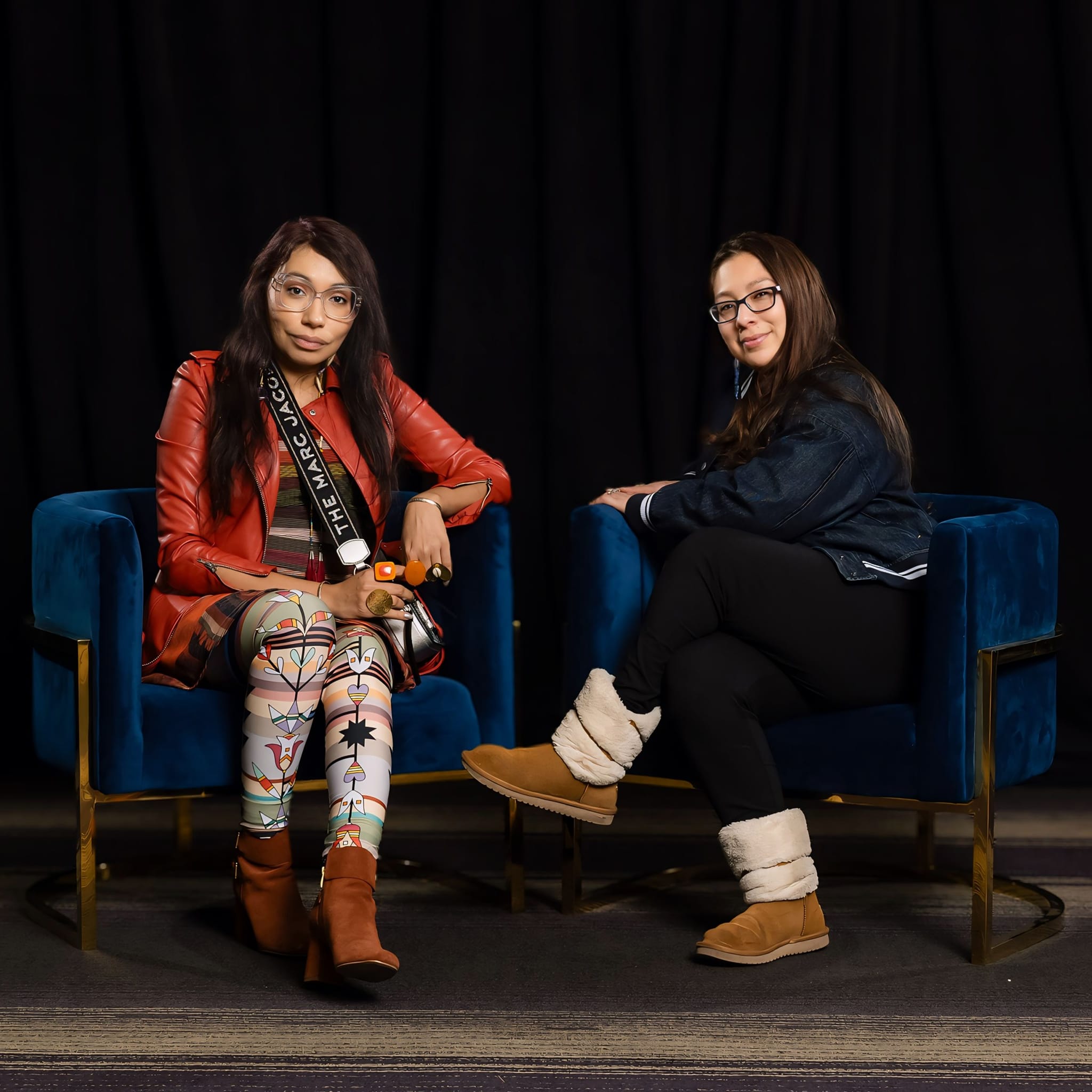 Dakota artists Marlena Myles and Tara Perron sitting together on blue chairs smiling towards the camera.