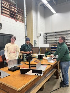 Three people standing in a workshop smiling and working on machines