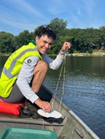 Person in a lime green vest smiling and holding a string in a boat on the lake. 