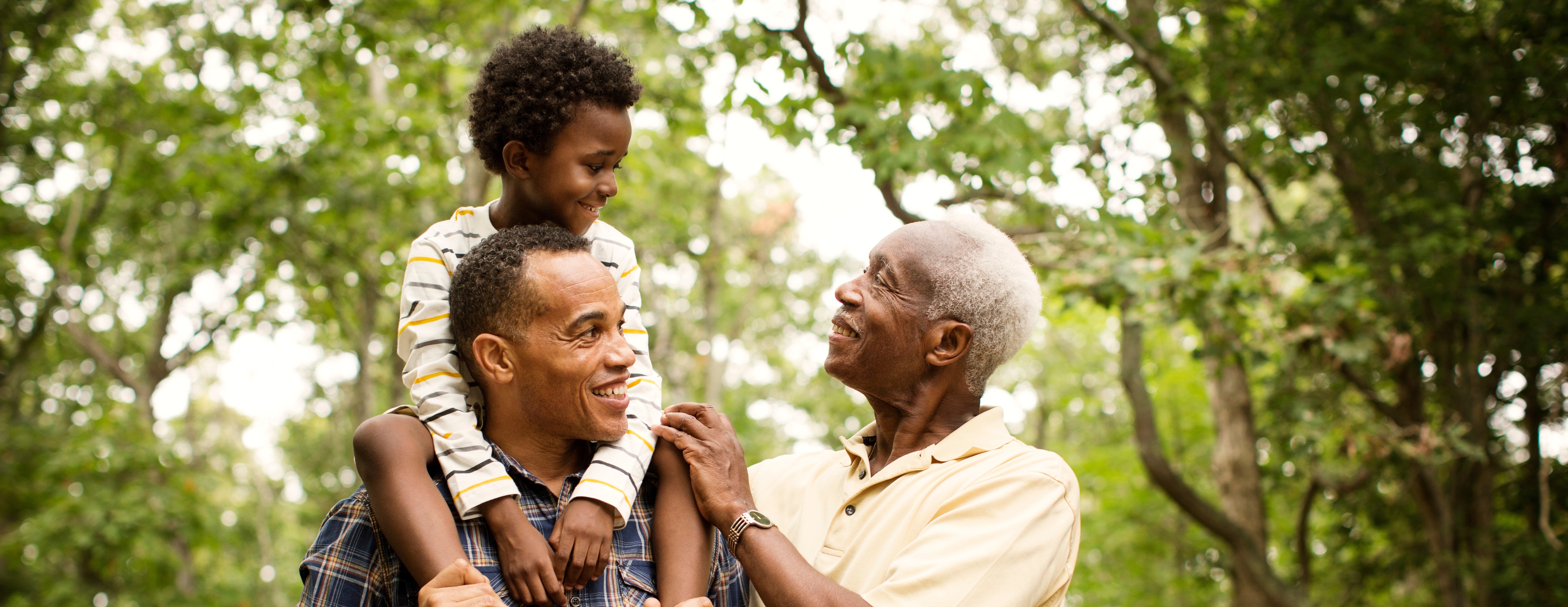 A child carried on an adult's shoulders while a gray haired adult looks on.