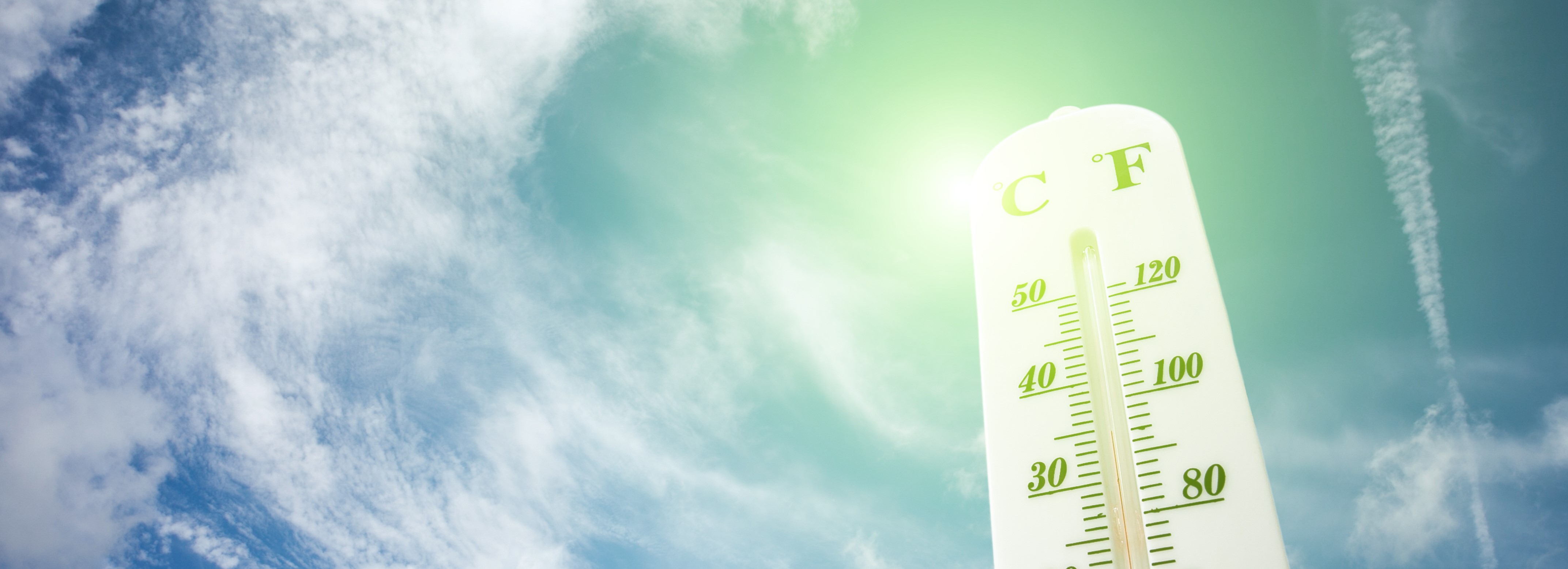 Image: A white thermomenter with black writing measuring Celsius on the left and Farenheight on the right reads 35 degrees Celsius or 94 degrees Fahrenheight. Behind the thermometer, the sun shines in a blue sky with some clouds.