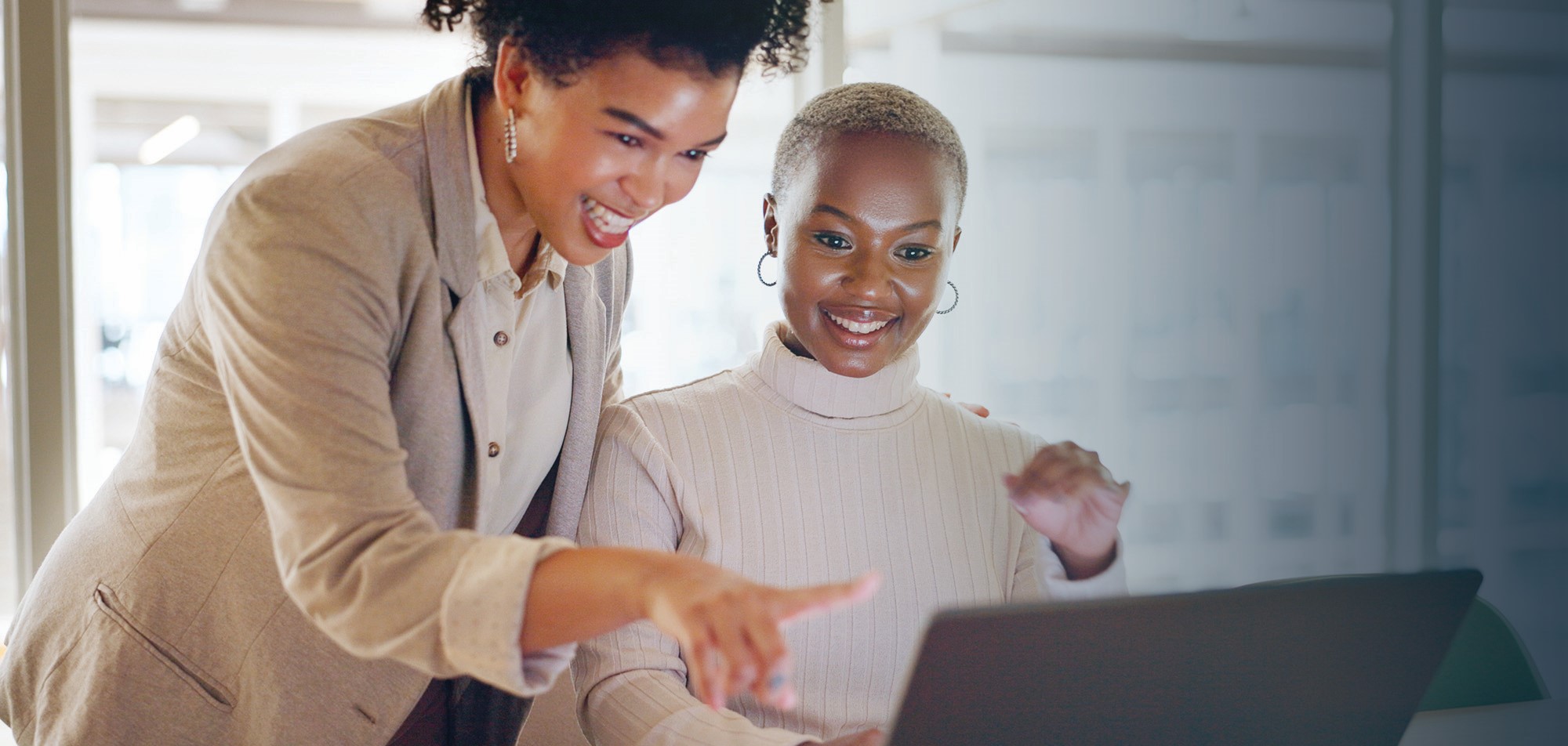 Image: Two women in business attire look at a laptop screen. One is pointing at the screen.