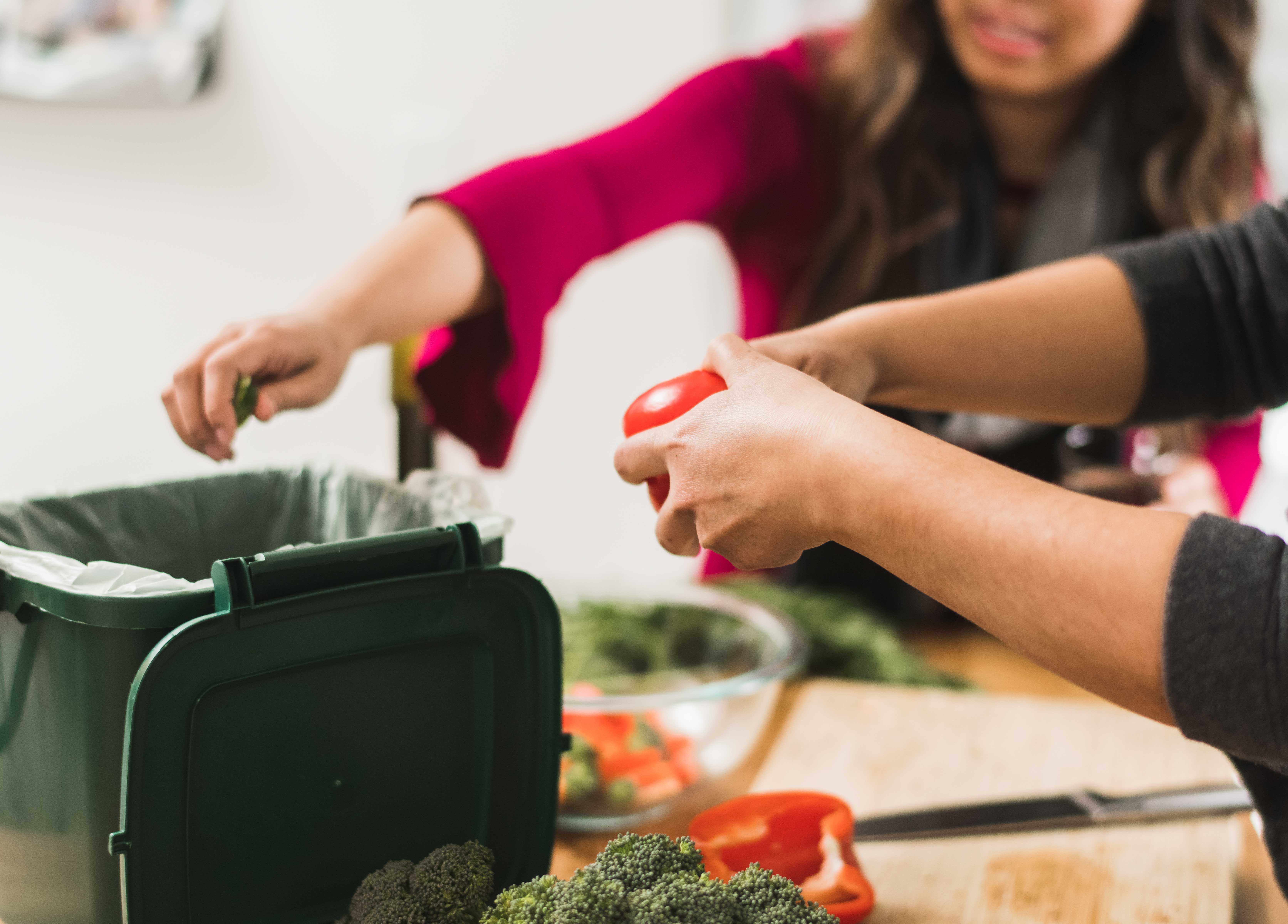 Two friends cooking and putting veggie peels in food scraps container