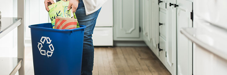 Woman putting cardboard in recycling container in brightly lit kitchen