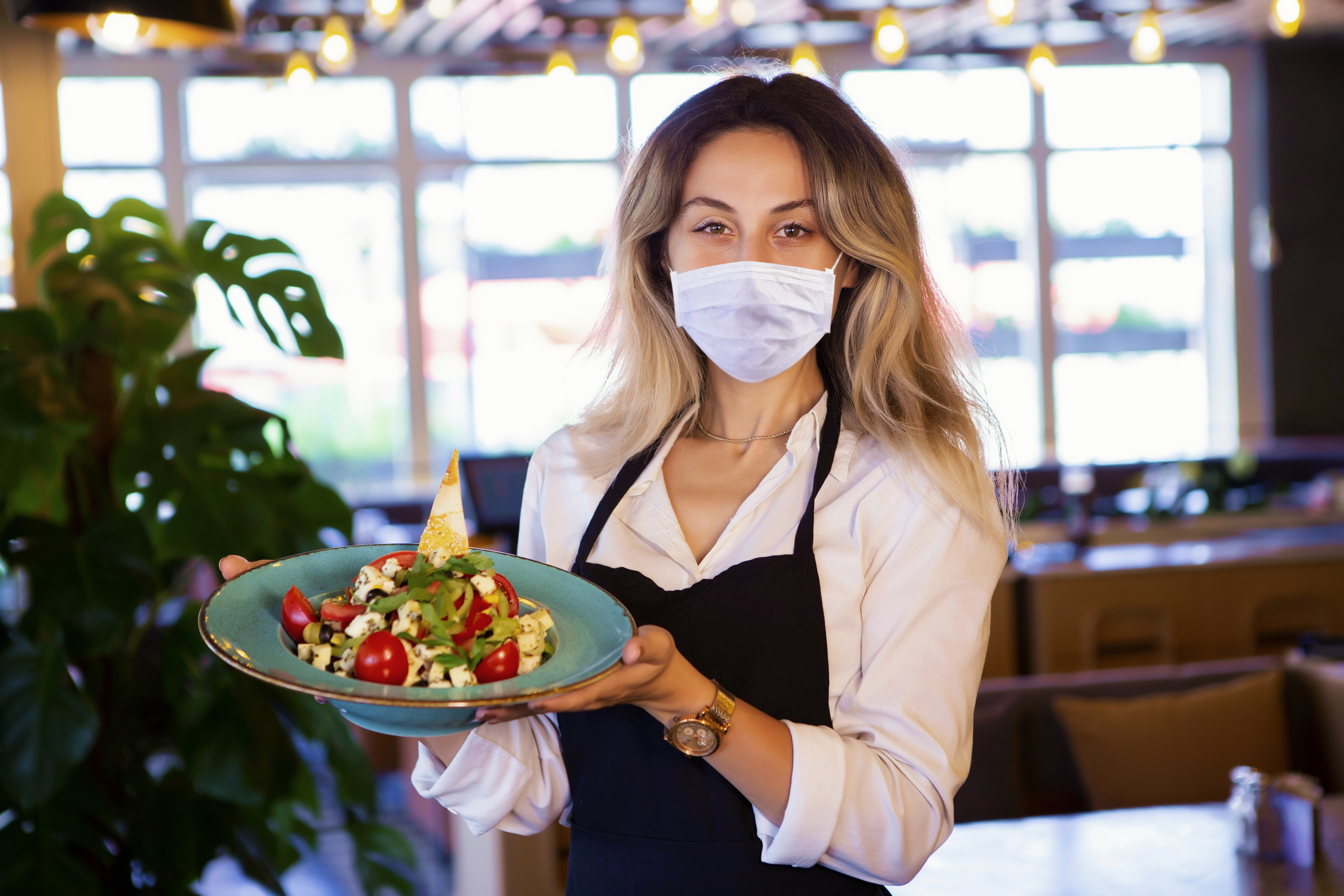 Restaurant server holding a plate and wearing a mask.