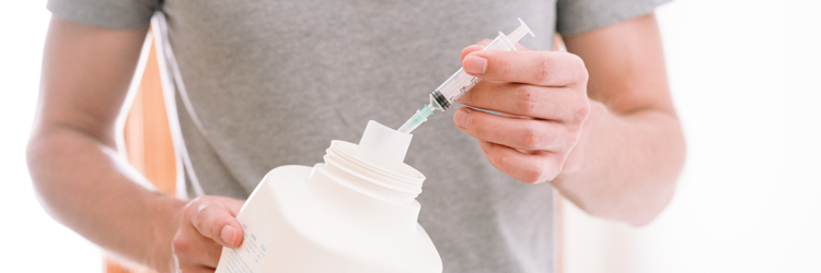 Torso and hands of a person placing a capped, empty syringe into an empty laundry detergent bottle.