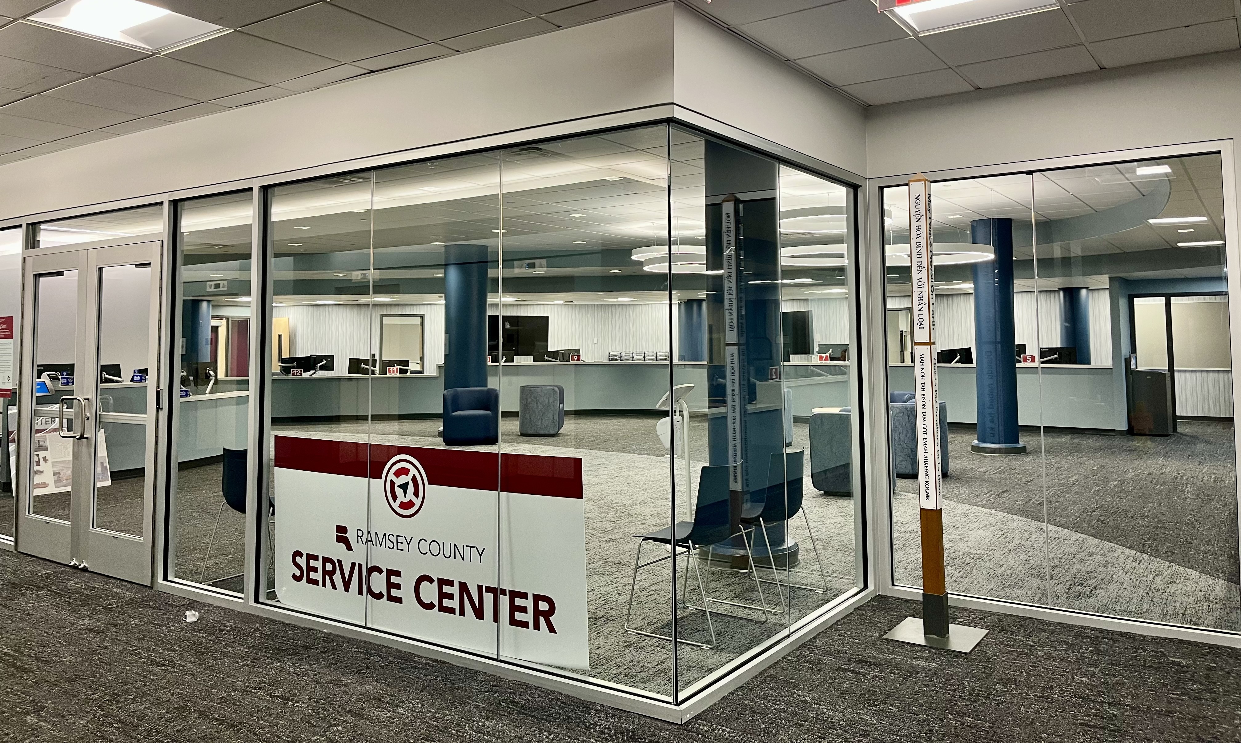Glass-walled Ramsey County Service Center with visible front desk, seating area, and modern lighting inside a clean, carpeted space.