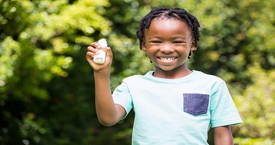 Smiling child holding up an asthma inhaler