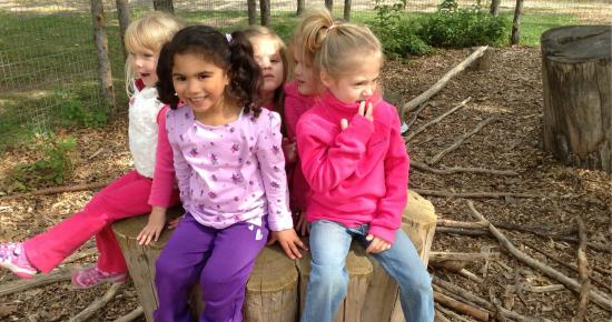 Smiling children sitting on a tree stump at Tamarack Nature Center