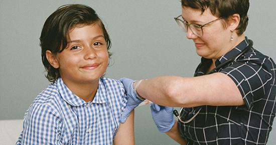 Young boy receives a vaccination while smiling at the camera_ by SELF Magazine and the American Association of Pediatrics