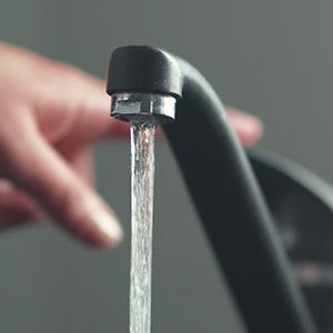 Tap water flowing from a faucet. In the background a hand is seen on the tap.